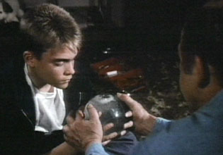 A boy with light hair looking intently at a glass snow globe held in an adult's hands.